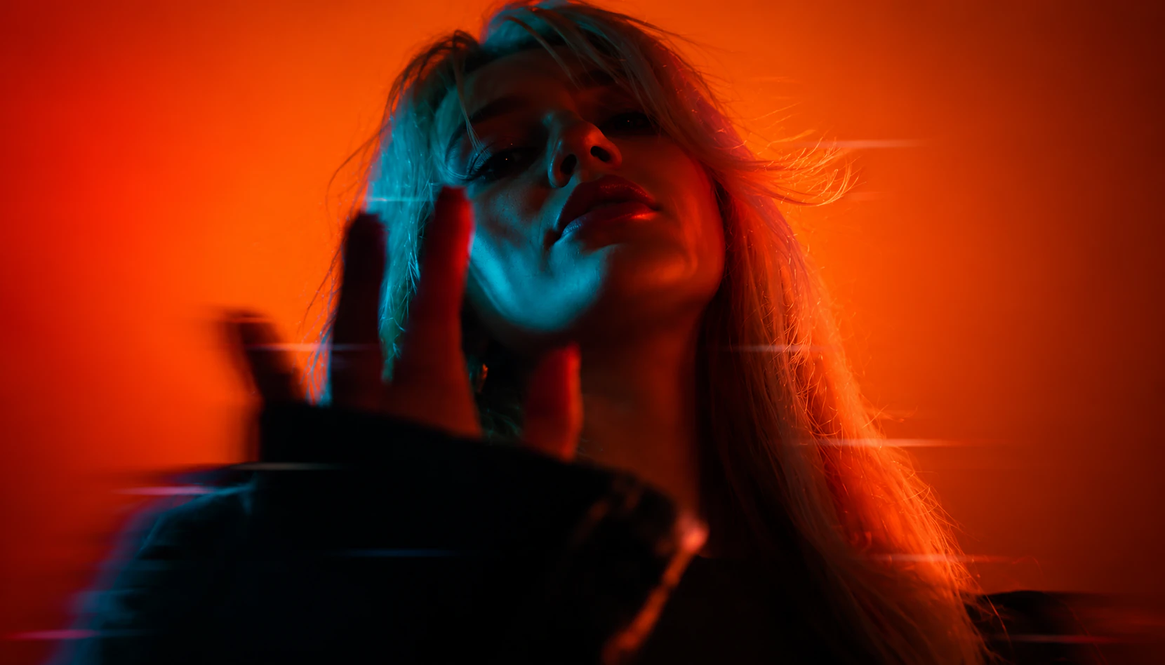 Woman with her hand raised, lit blue against a glowing orange backdrop